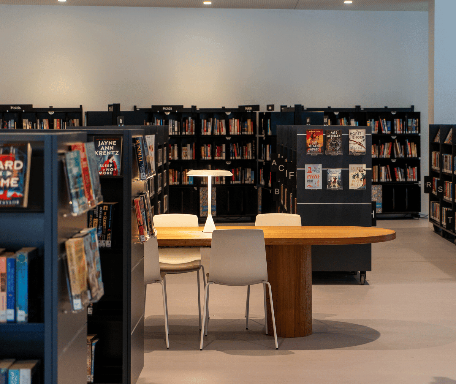 Photo of reading area inside the Ballarat Library. Shelves of books surround a table with a lamp on it.