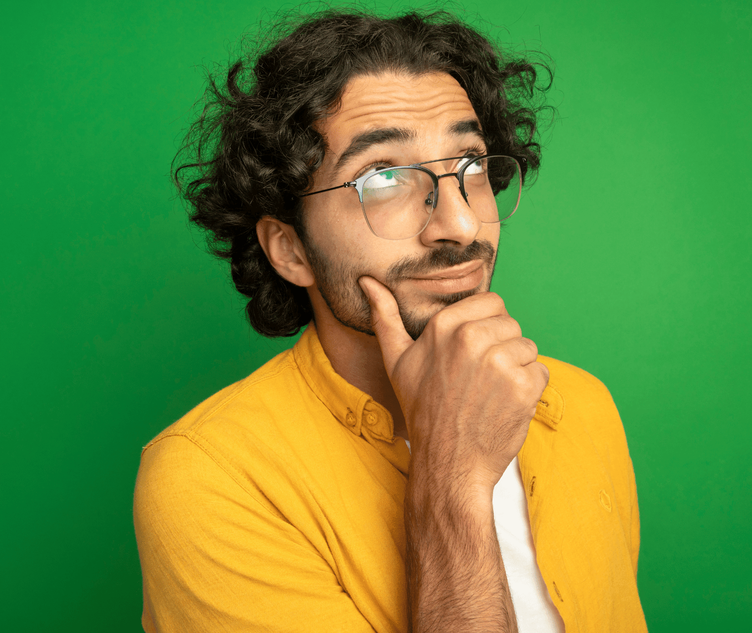 A man wearing a yellow shirt poses with his hand on his chin against a green background.