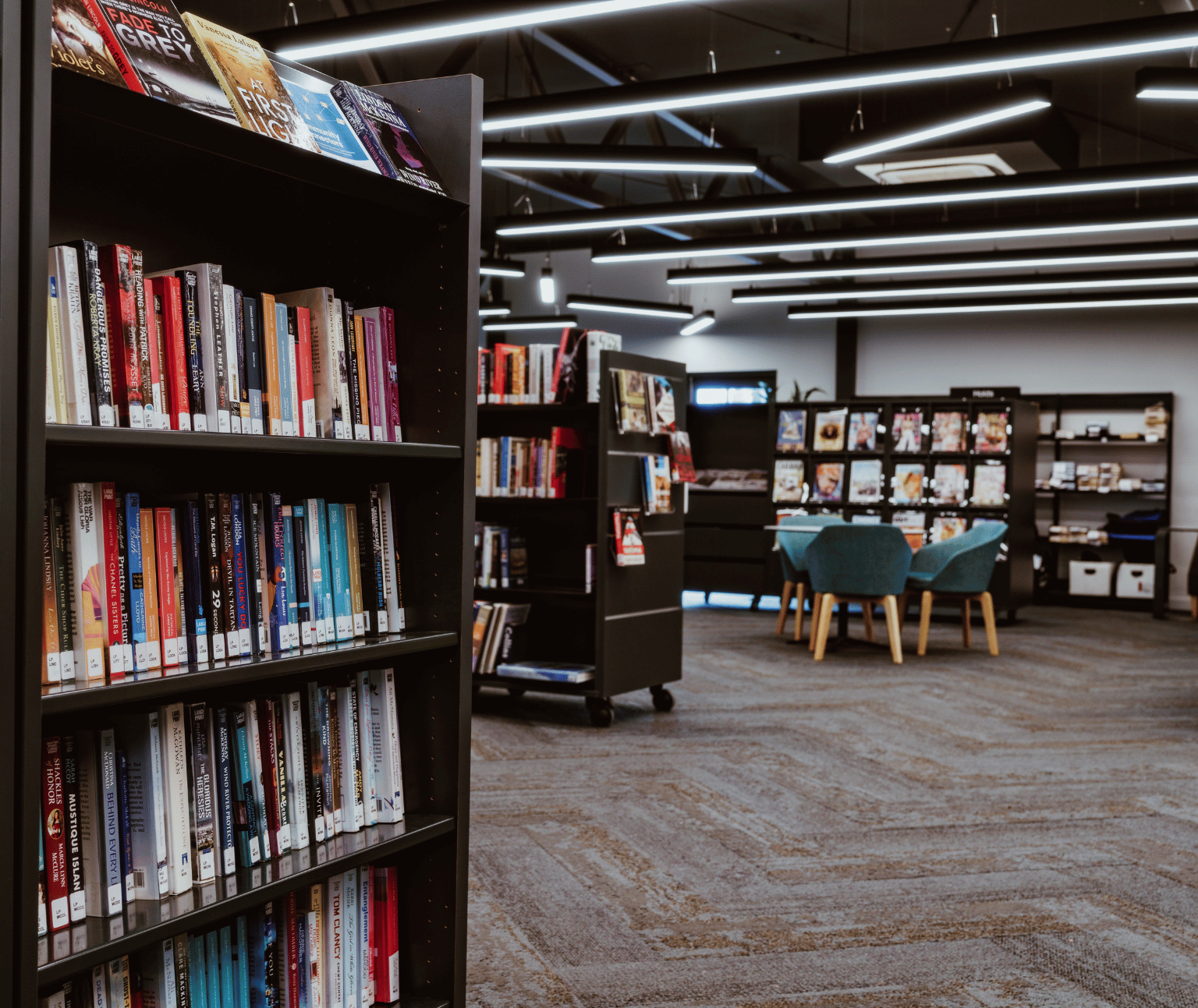 Looking past shelves of books at Sebastopol Library. There is a round table with green upholstered chairs around it.