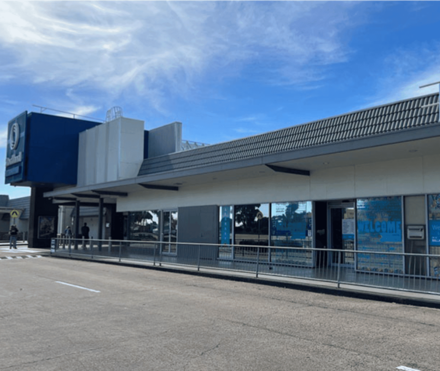 External picture of Wendouree Library. Blue writing on the windows read 'Welcome'. There is a metal fence in front of a footpath leading to the entrance.