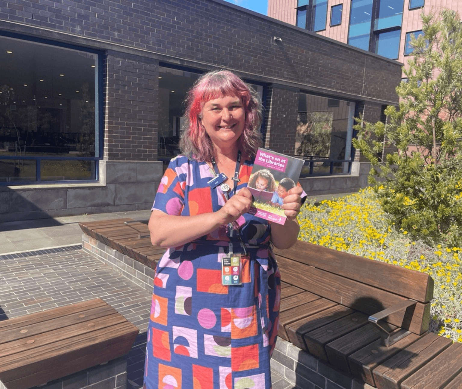 Photo of library staff member holding a copy of the What's On brochure in the courtyard at Ballarat Library.