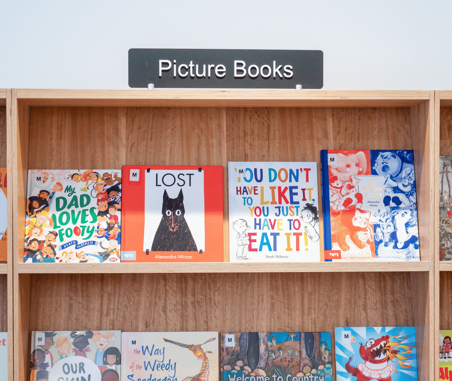 Four picture books with bright covers sit against a wooden shelf.