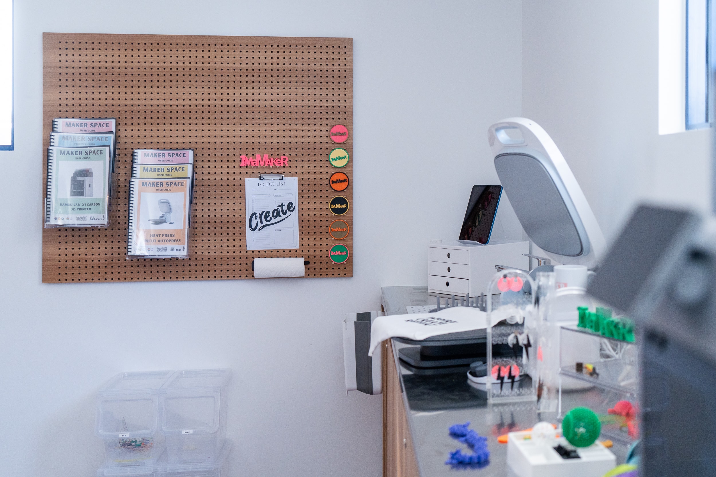 A photo of the Maker Space featuring a heat press, 3D printed objects and a pegboard of Maker Space guides.