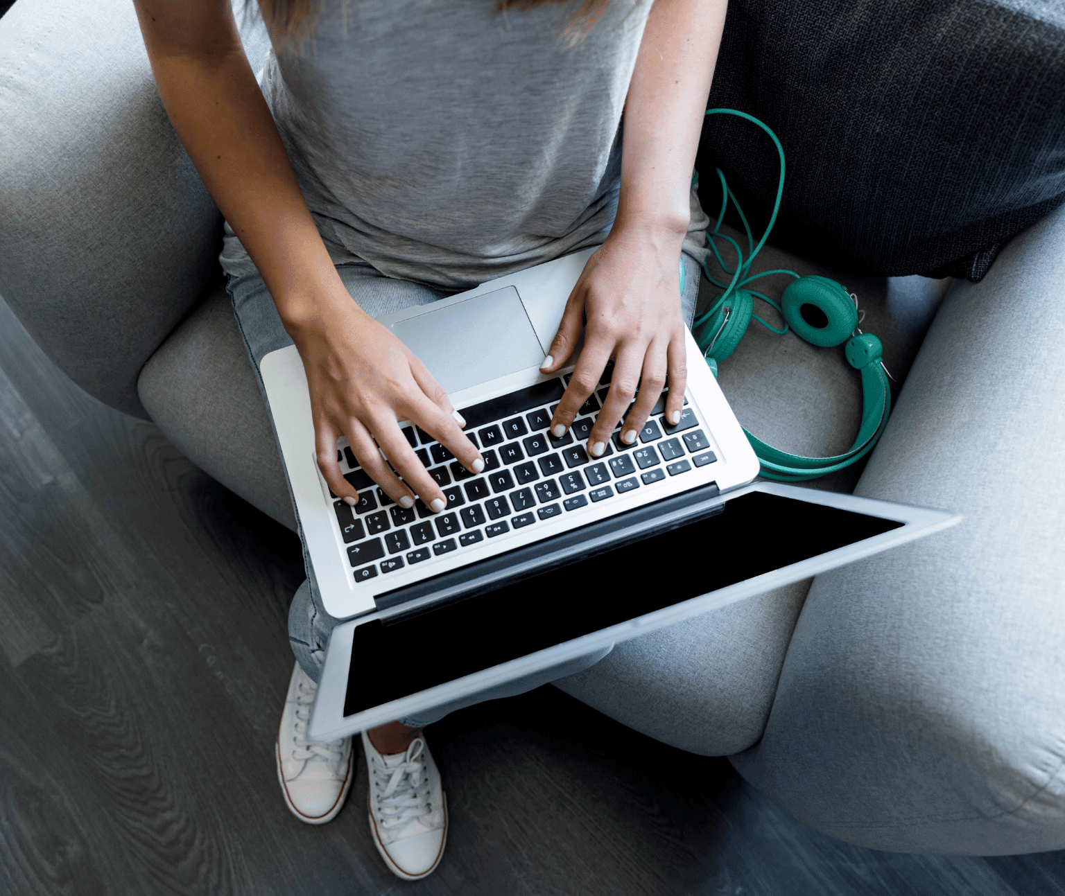 View of a persons hands typing on a laptop. There are green headphones to the side.