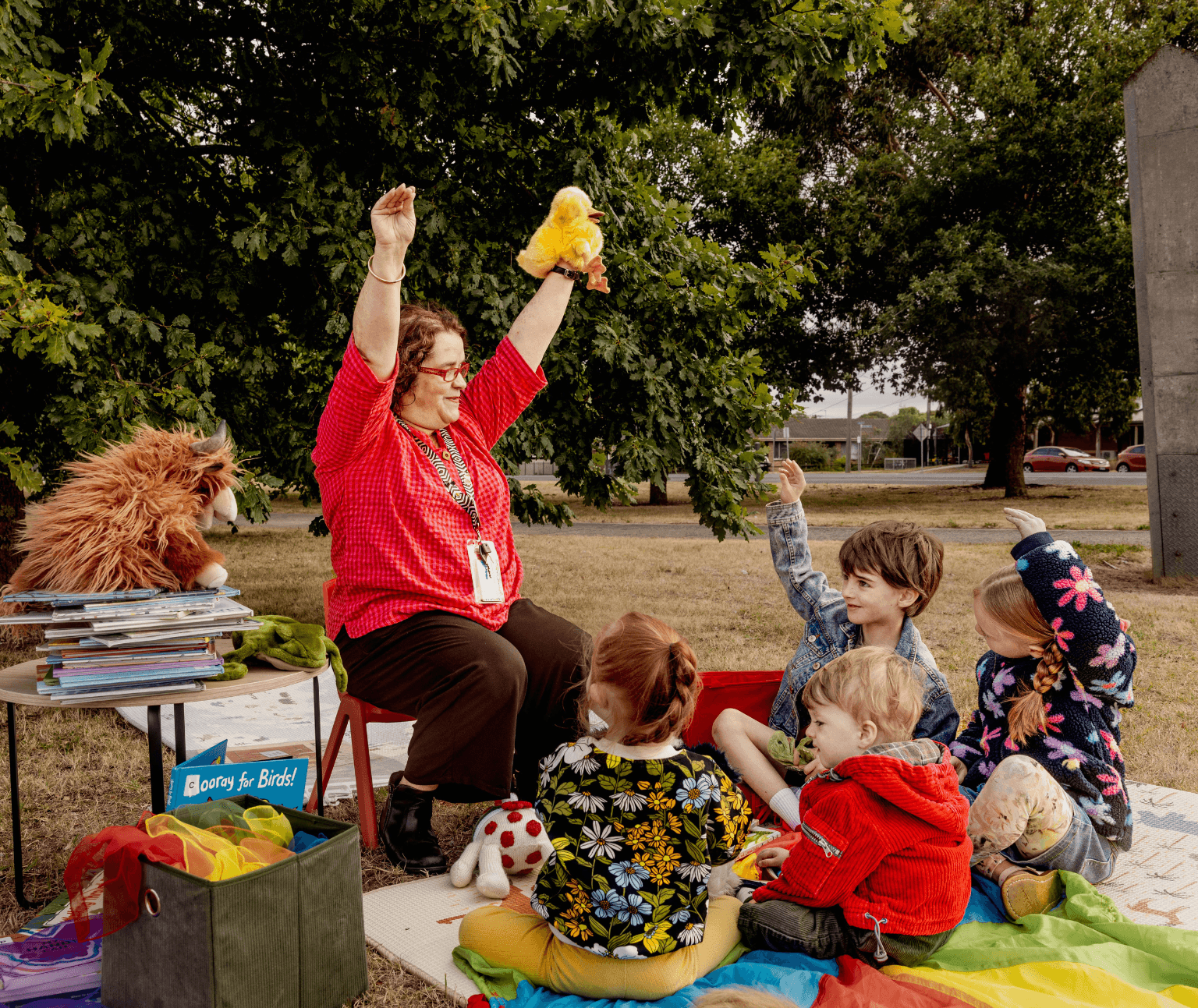 Photo of a librarian performing storytime with a small group of children in a park.